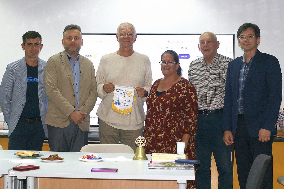 Sześcioro uczestników spotkania klubu Rotary Warszawa-Belweder; pośrodku mężczyzna trzyma proporczyk Rotary Club Anaheim, CA