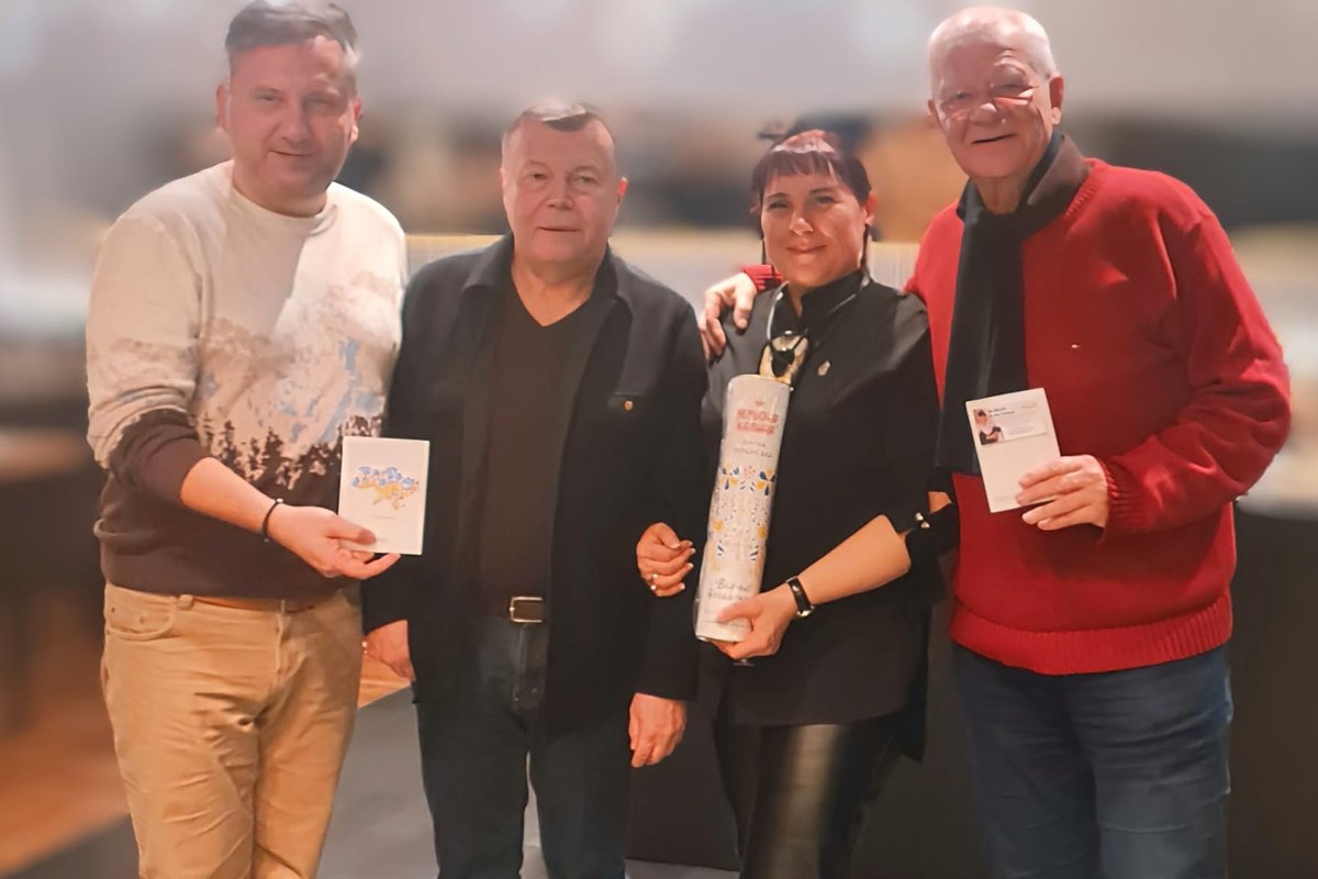 Czworo uczestników spotkania pozuje do zdjęcia; pośrodku Olha Paliychuk z upominkiem w ręku