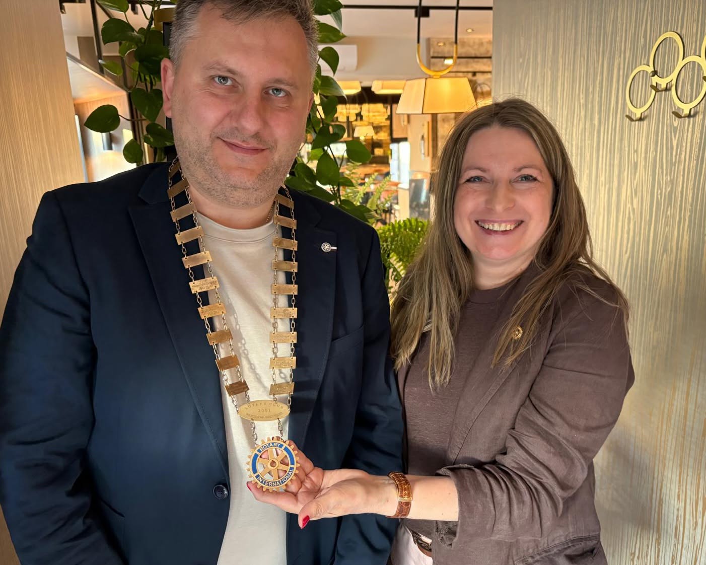 Prezydent Klubu w prezydenckim łańcuchu obok ustępującej prezydentki, oboje trzymają emblemat Rotary International