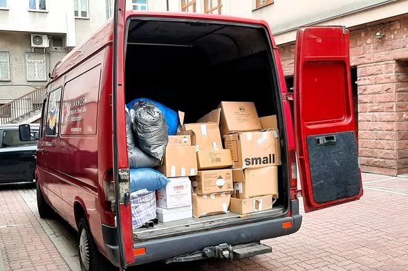 Otwarty tył czerwonego busa wypełnionego kartonami i workami z pomocą humanitarną